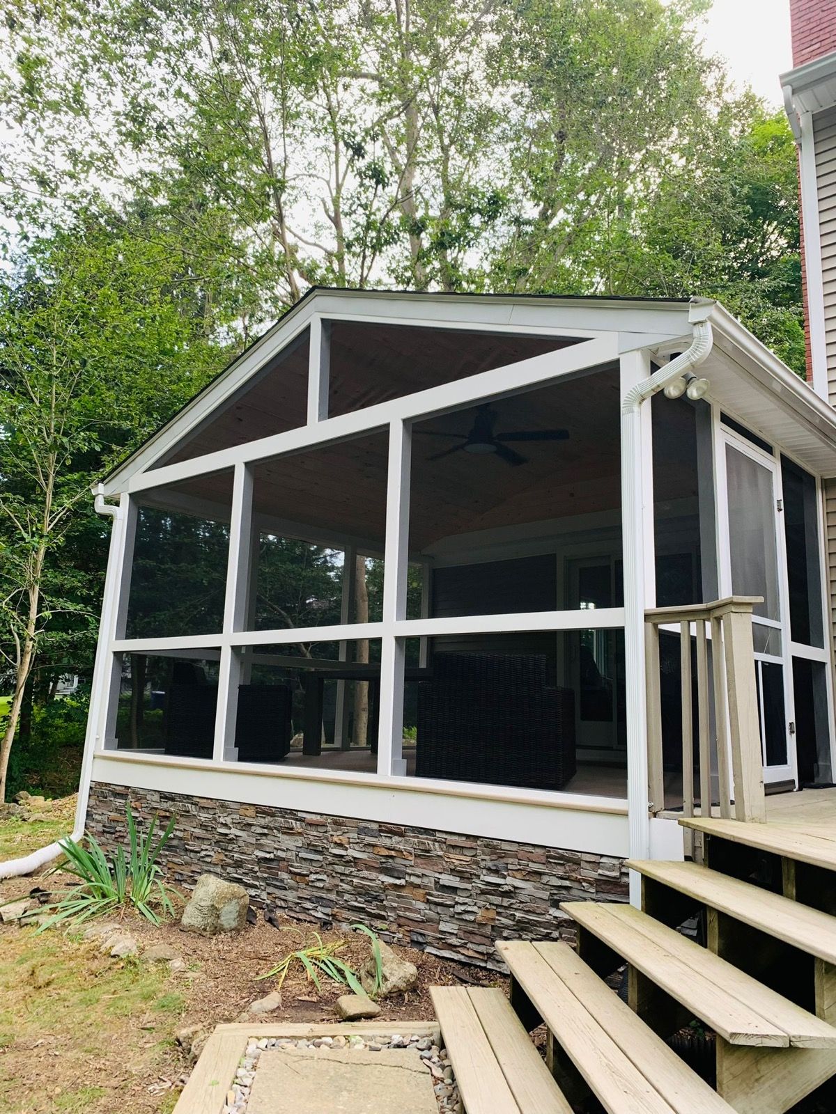 Enclosed sunroom addition seen from the yard with glass walls and steps.